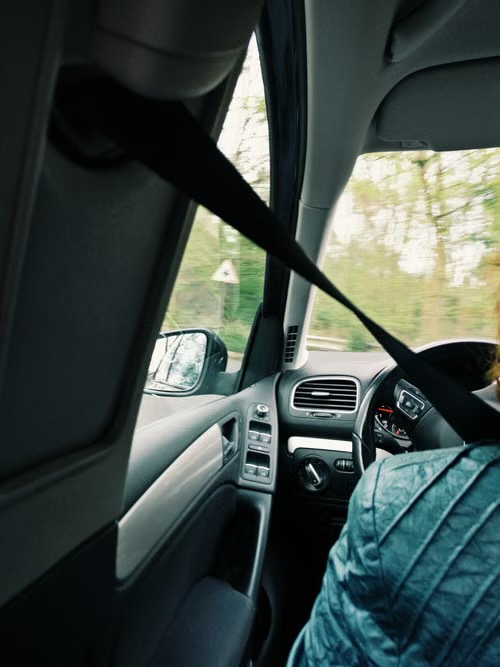 Interior view from a rear seat while the vehicle is moving, with the shoulder belt worn and the road blurred outside.
